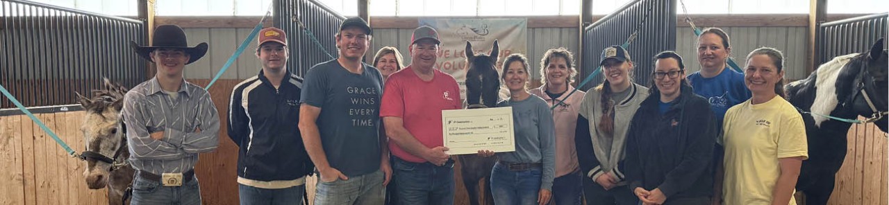 P1 Project Manager Jack Kobe in the center, surrounded by members of Great Plains Adaptive Riding Academy in a barn with horses